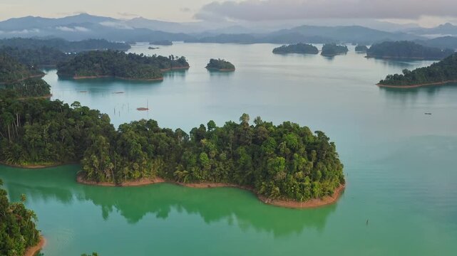 Breathtaking aerial view of Cheow Lan Lake turquoise waters and lush rainforest islands framed by dramatic limestone karsts in Khao Sok National Park, Thailand. Nature landscape. Drone flight panorama