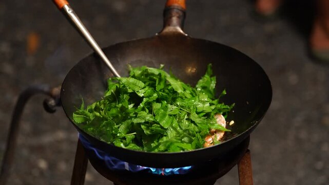 Traditional thai food, Wok spinach flame cooking vegetable pan stove kitchen heat food preparation with green leaf meat blue gas fire stir fry steam fresh herb hot metal outdoor rustic