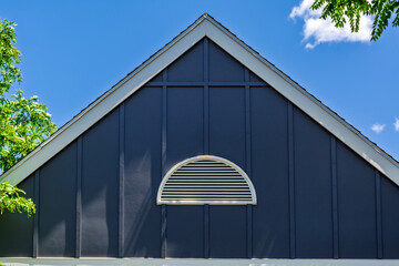 Upper gable of a house with blue siding and a white half-round vent against a blue sky  © Baharlou