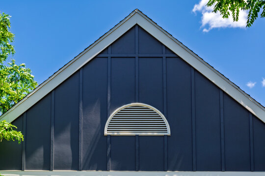 Upper gable of a house with blue siding and a white half-round vent against a blue sky
