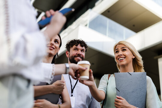 Group of cheerful professionals interacting outdoors with coffee