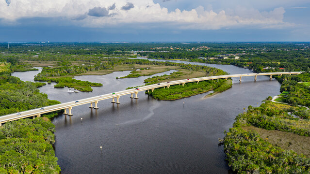 An aerial view of the Fort Hamer Bridge over the Manatee River in Bradenton, Florida. Afternoon rain showers fill the dark sky in the distance.