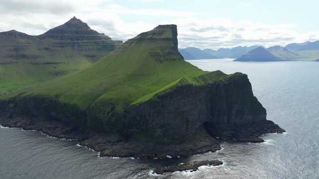 Dramatic aerial pull back drone shot revealing the stunning landscape of Island Kalsoy, part of the Faroe Islands. The cliffs are the location of Kallur Lighthouse and the grave stone of James Bond.