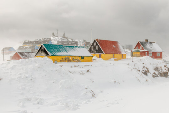 Colorful wooden houses in Paamiut during a snowstorm with deep snow, foggy hills and traditional Greenlandic village scenery, Paamiut, Sermersooq, Greenland