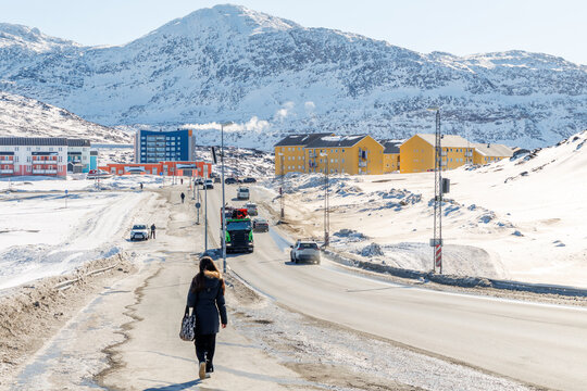 Winter street scene in Nuuk with pedestrian, cars, yellow apartment buildings, snowy roadside and rugged polar mountains, Nuuk, Sermersooq, Greenland