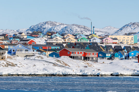 Winter waterfront view of Ilulissat with colored houses, snowy hills and quiet arctic water in Ilulissat, Avannaata, Greenland with snow, ice and coastal arctic winter scenery