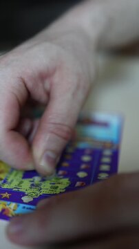 Vertical screen Hand scratches lottery ticket with coin revealing hidden symbols during exciting game of chance hoping for jackpot lucky win and instant prize today
