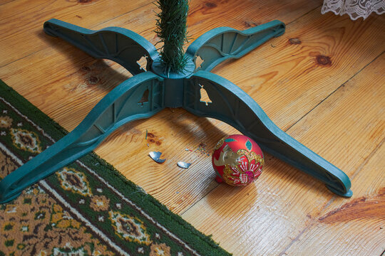 Broken Christmas toy on wooden floor, Broken red Christmas ornament on a wooden floor under the tree stand