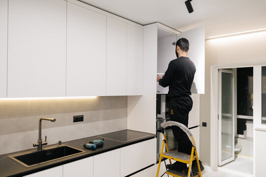 Professional worker installing white custom kitchen cabinets in a modern residential apartment interior renovation project