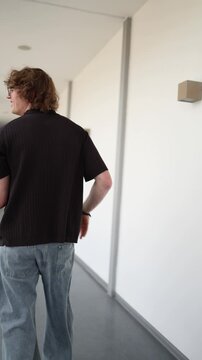 Vertical screen Careless software developer walks away scratching himself while carrying laptop showing sloppy workplace habits and unprofessional office behavior