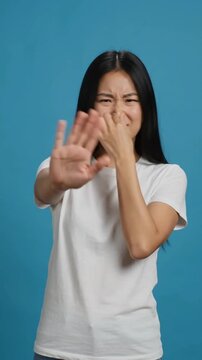Displeased woman reacts to bad smell in indoor setting with blue background