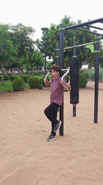 Teenage boy performing dips on parallel bars at an outdoor fitness park. Active adolescent doing bodyweight strength training in a public sports area surrounded by greenery. Healthy lifestyle, youth f