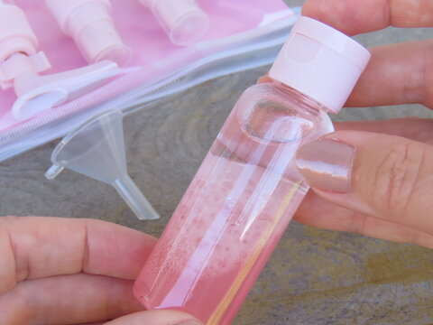 Woman hands holding a travel set plastic bottle with bi-phase oil inside. Female hands preparing travel set containers.