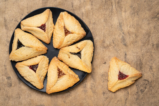 hamantaschen pastry with apricot, raspberry and prune filling on a black ceramic plate against handmade bark paper, a traditional pastry in Ashkenazi Jewish cuisine for holiday of Purim