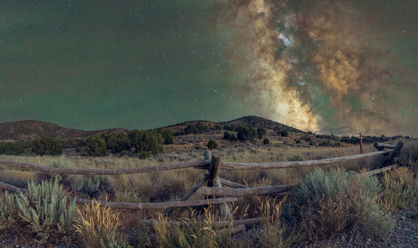 View of the Milky Way galaxy stretching over the desert landscape and a rustic wooden fence along the historic Pony Express Trail near Dugway, Utah, United States.