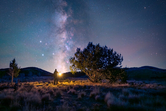 View of a person holding a lantern under the Milky Way galaxy in the desert landscape near Dugway, Utah, United States.