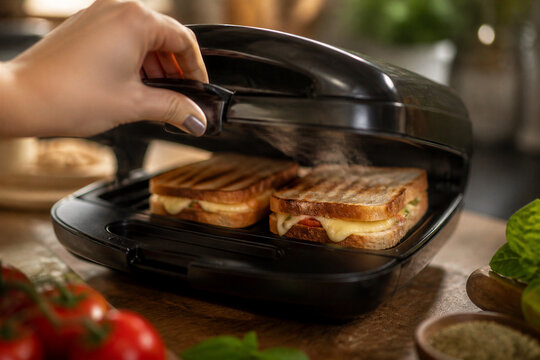 Hand lowering grilled sandwiches into kitchen counter sandwich press