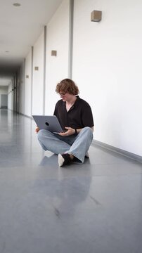 Young freelancer sits on the office floor with a laptop feeling confused after a work setback searching for solutions solving problems and trying to finish a project