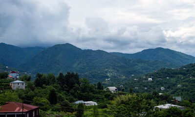 Obraz premium Rural house on a lush green hillside with a mountain village and blue sky in the background