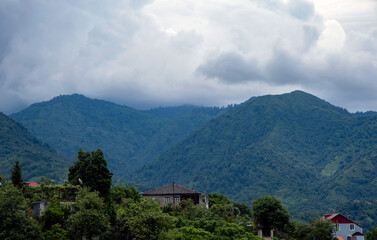 Obraz premium Mountain landscape under dramatic storm clouds with rural houses nestled in lush green hills