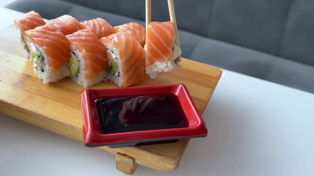 A classic Philadelphia roll wrapped with fresh salmon is gently dipped into dark soy sauce served in a red rectangular dipping dish