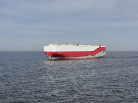 Massive RoRo car carrier ship sailing at full speed on the open sea. Huge vessel cuts through blue water leaving a wake. Powerful view of maritime transport and global vehicle logistics.