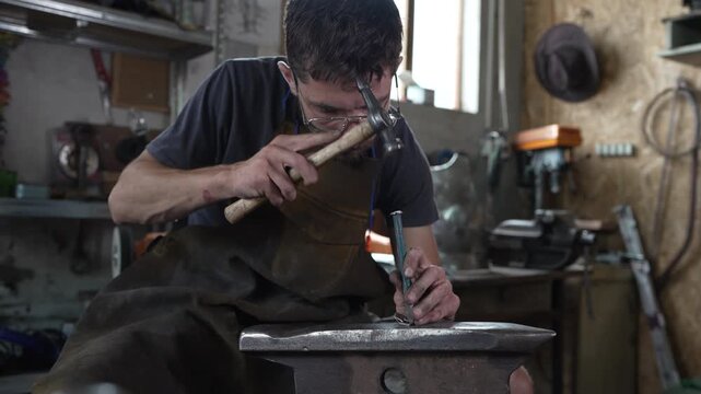 Blacksmith hammering a metal punch on an anvil in a workshop