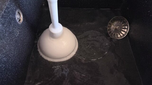 Person's hands using a white rubber plunger to clear a slow kitchen sink drain