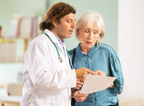 Adult man physician explaining laboratory results to elderly woman during consultation in clinic