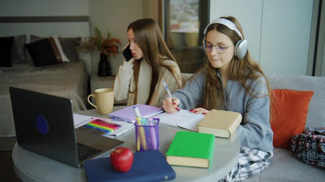 Two teenagers studying at a table in a modern room with books, a laptop, and school supplies during a weekday afternoon