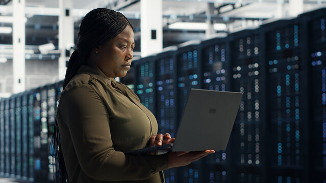 Systems engineer working with notebook computer in server facility, integrating new technologies and systems.