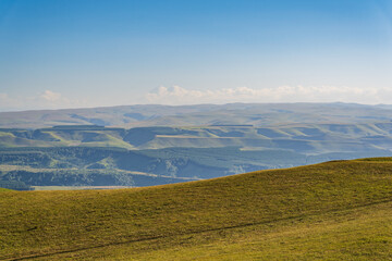 Fototapeta premium Panoramic view of the green valley and the snowy peak of Mount Elbrus on the horizon against the blue sky on a sunny clear morning in Kislovodsk Stavropol territory, Russia