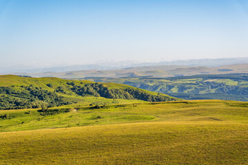 Fototapeta premium Layers of green mountains and hills in the haze during sunset. Panoramic View of Green hills and Meadow.