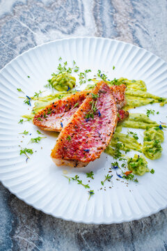 Fried mullet fish fillet with fresh artisan avocado cream guacamole served as close-up on a design plate