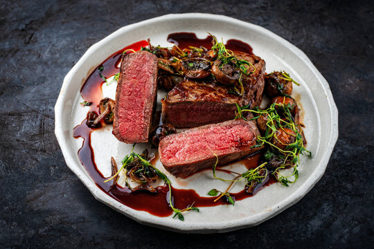Traditional barbecue grass-fed dry aged roast beef steak tagliata with grilled mushrooms and fresh greens and herbs served as close-up on a design plate