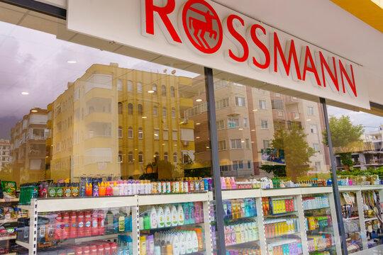 Rossmann retail store exterior in Alanya, Turkey, view featuring shelves of various products and a prominent sign above the entrance, reflecting nearby buildings in the glass facade