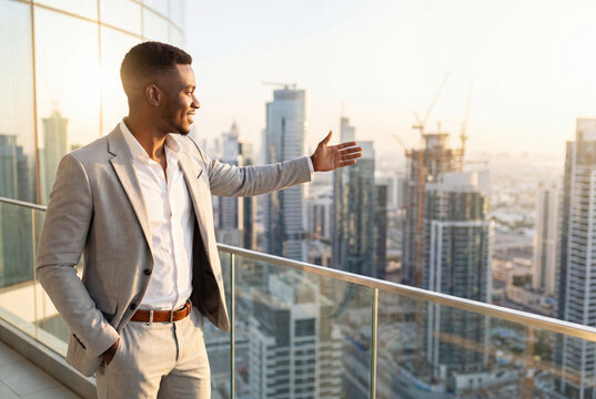Smiling businessman gesturing toward expanding city skyline from high rise balcony