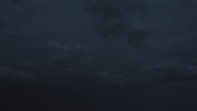 Dark thunderstorm clouds glowing with sudden lightning at night