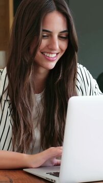 Beautiful freelancer smiling and typing on a laptop computer keyboard, working from home