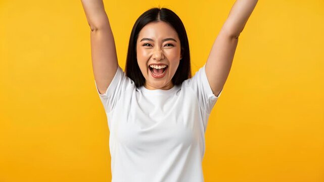 Exuberant Celebration: A young woman with an infectious smile raises her arms in a gesture of pure joy and triumph against a vibrant yellow backdrop.