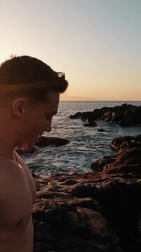 Young athletic man taking a selfie video as he jumps backwards from rocks into the ocean at sunset