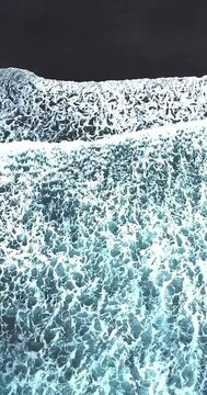 Foamy ocean waves washing over a volcanic black sand beach creating an abstract natural texture
