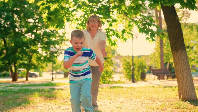Young son plays with mom, running together summer park. Family run. Laughing little boy runs away from mom outdoors. Carefree childhood. Small child fun outdoors with mama in summer. Baby mom laughing