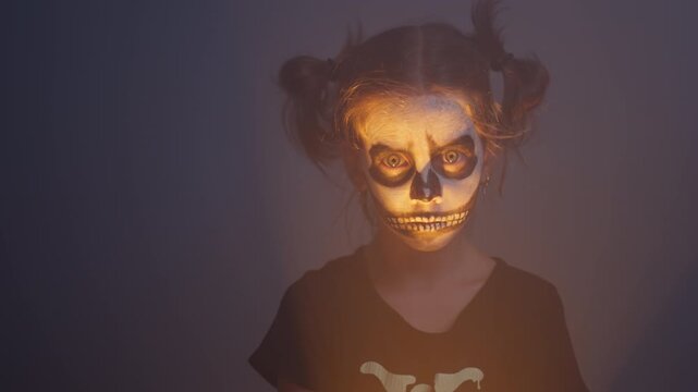 Girl wearing skeleton costume and face paint holding torch. Zoom in shot of little child looking towards camera with spooky expression creating Halloween mood
