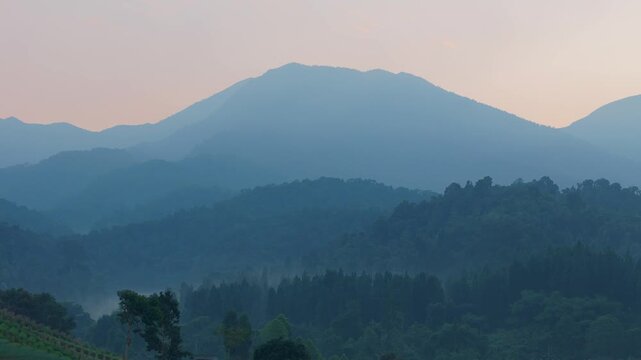 Aerial view of misty mountains and lush forests at sunrise in West Java, Indonesia.
