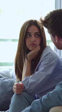 Worried couple talking on the sofa while dealing with relationship issues, the sad girlfriend listens as her boyfriend tries to comfort her during a difficult conversation at home