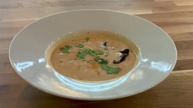 Creamy mushroom puree soup white plate on wooden table restaurant closeup, garnished with herbs and mushroom slice, warm natural