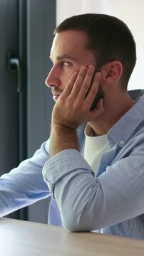 Melancholic young man sitting at a desk with his head in his hand, feeling bored and tired. Unhappy male student or remote worker dealing with burnout, stress, and lack of motivation