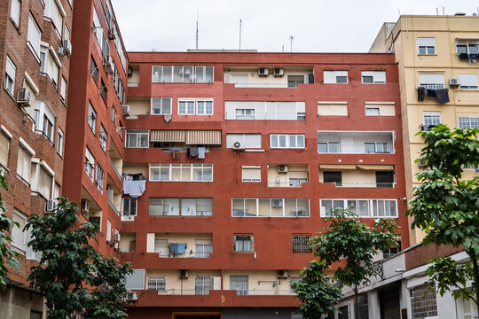 Dilapidated social housing block in Valencia, Spain, worn red facade, enclosed balconies, air conditioners and laundry, showing urban housing conditions, residential density and Spanish real estate.