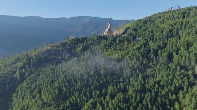 Aerial view of the giant Buddha Dordenma statue perched on a lush green forested hillside overlooking the valley in Thimphu, Thimphu, Bhutan.